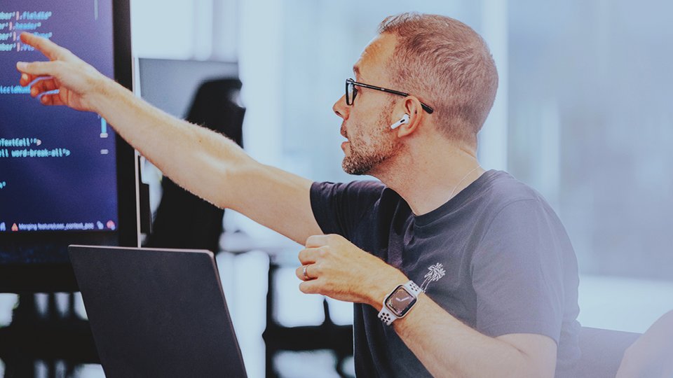 A software developer points to a code on a screen during a meeting.
